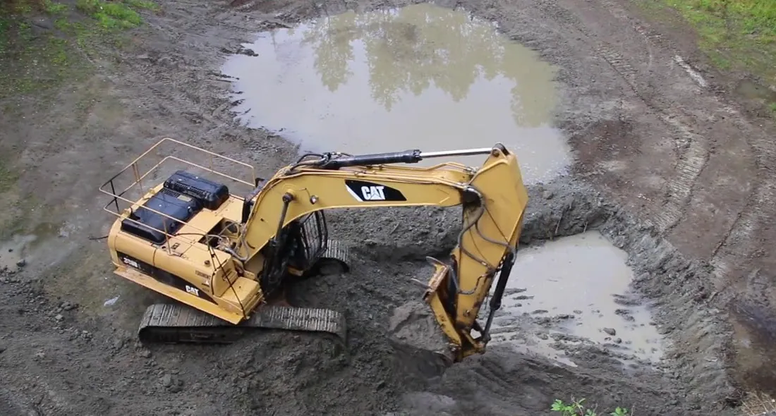 Excavator digging a new pond basin below grade as ground water seeps into the bottom