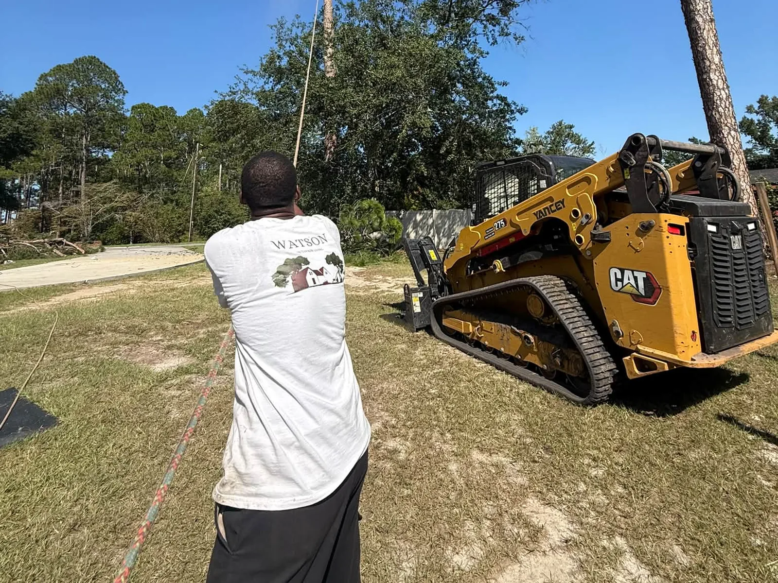 Crew member guiding a pine with a rope beside the CAT 275 track loader